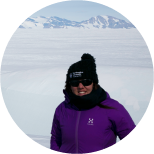 Kate Winter, smiling, in front a snow field rising to snow covered mountains in the distance