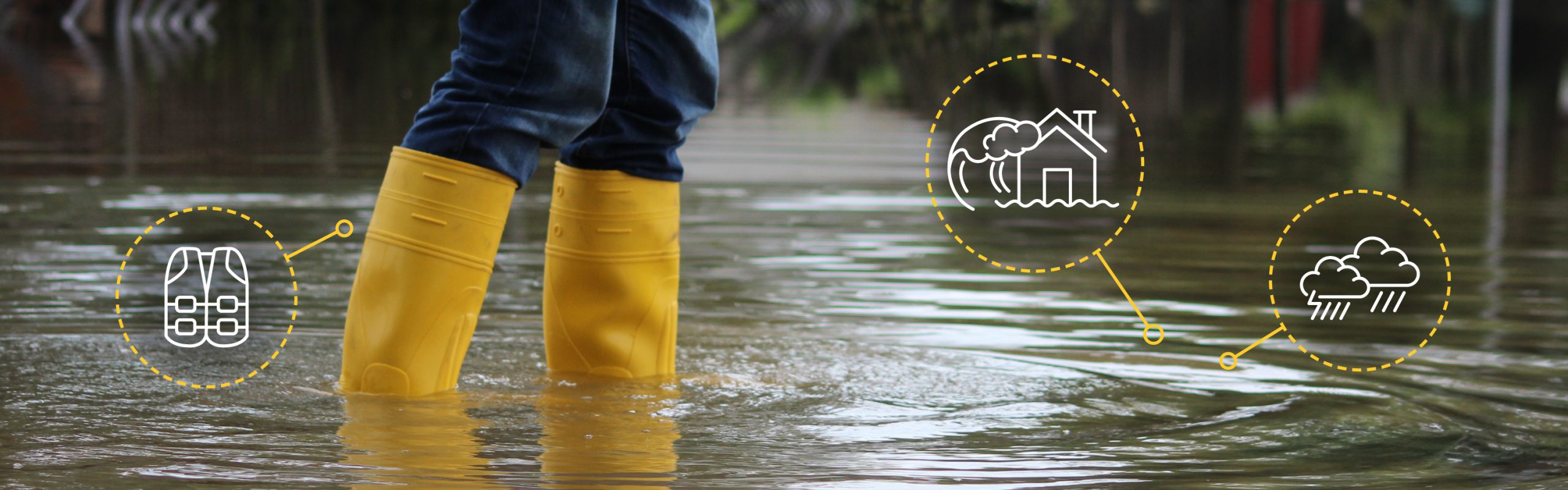 The lower half of a person, wearing wellington boots, standing in flood water.